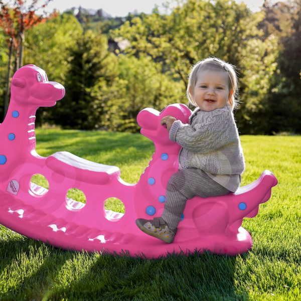 WOOPIE-Bujak-Wieloosobowy-Dino-Hustawka-Rownowazna-Rozowa-3 Różowa zjeżdżalnia dla dzieci w kształcie dinozaura na trawie w parku z dzieckiem bawiącym się na zjeżdżalni, idealne do zabawy na świeżym powietrzu i rozwoju motoryki u maluchów.